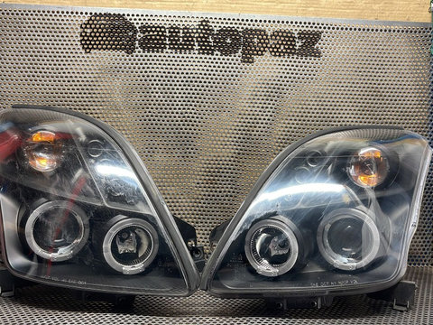 Set faruri aftermarket cu lupă și halogen Suzuki Swift 2005 (cel din dreapta are o prindere ruptă)